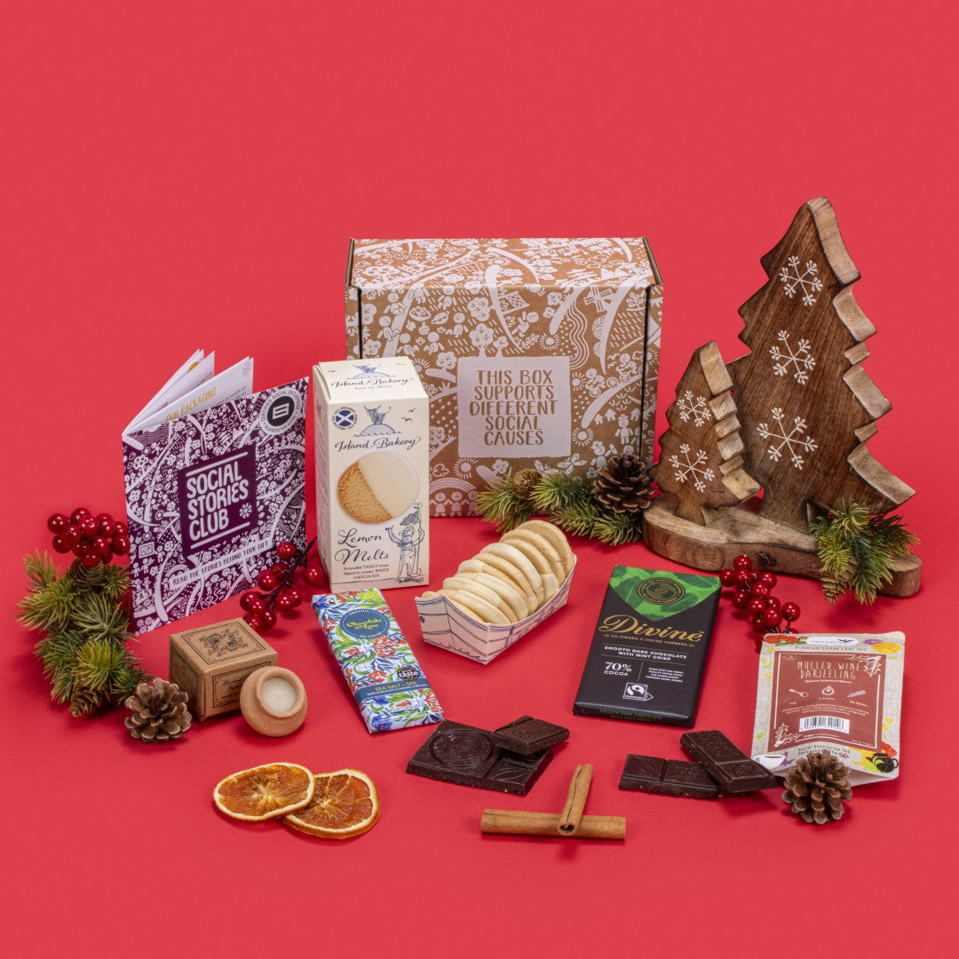 Secret Santa Gift Box open, displaying mulled wine tea, lemon melt biscuits, sea salt caramel chocolate, mint crisp dark chocolate, lavender candle, and story booklet, with festive pine cones and eco-friendly packaging.