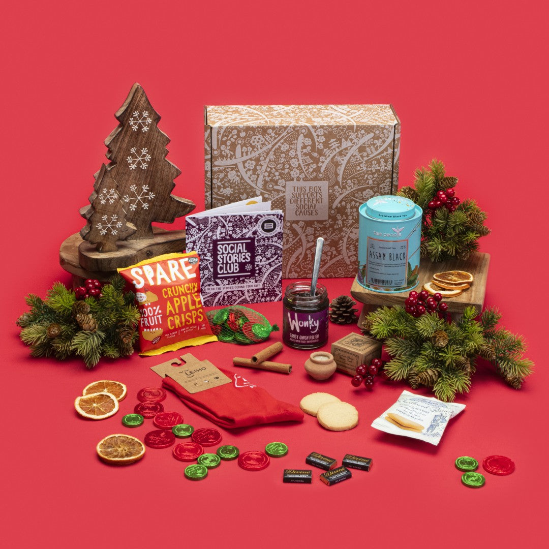 Sustainable Christmas Box open, showcasing Assam tea caddy, shortbread biscuits, dark chocolate napolitains and coins, lavender candle, apple crisps, onion relish, bamboo socks, with sustainable packaging and festive accents.