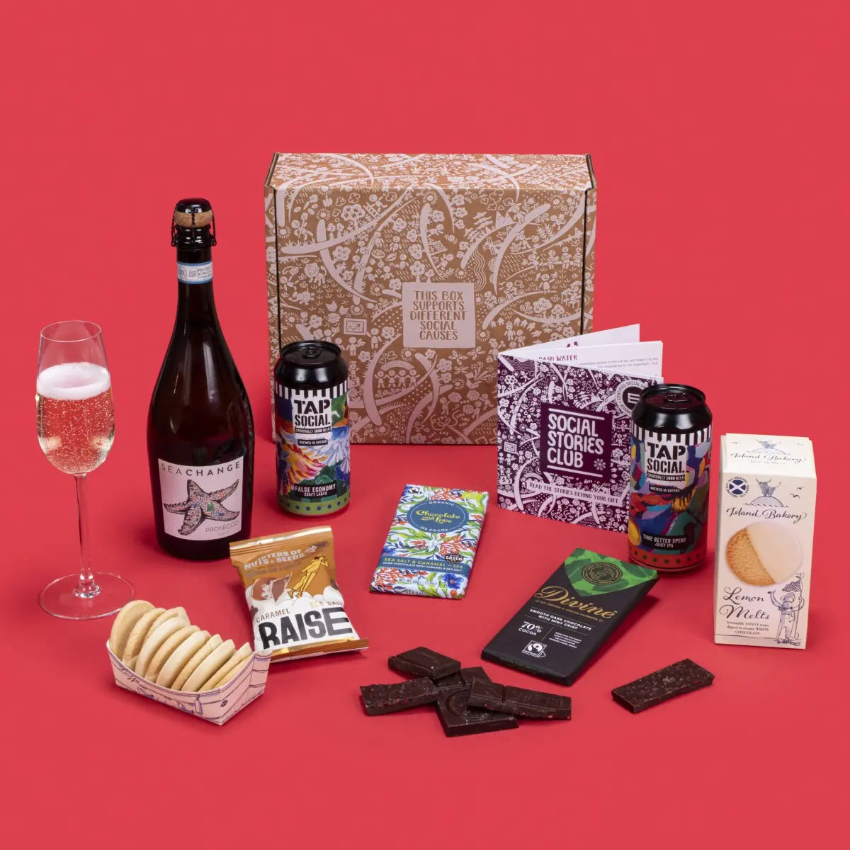 Celebration Gift Box open, featuring lemon melt biscuits, salted caramel and mint crisp chocolates, salted caramel nuts, choice of wine, craft lager, IPA, story booklet, and personalised note in vibrant sustainable packaging with wintery festive accents.