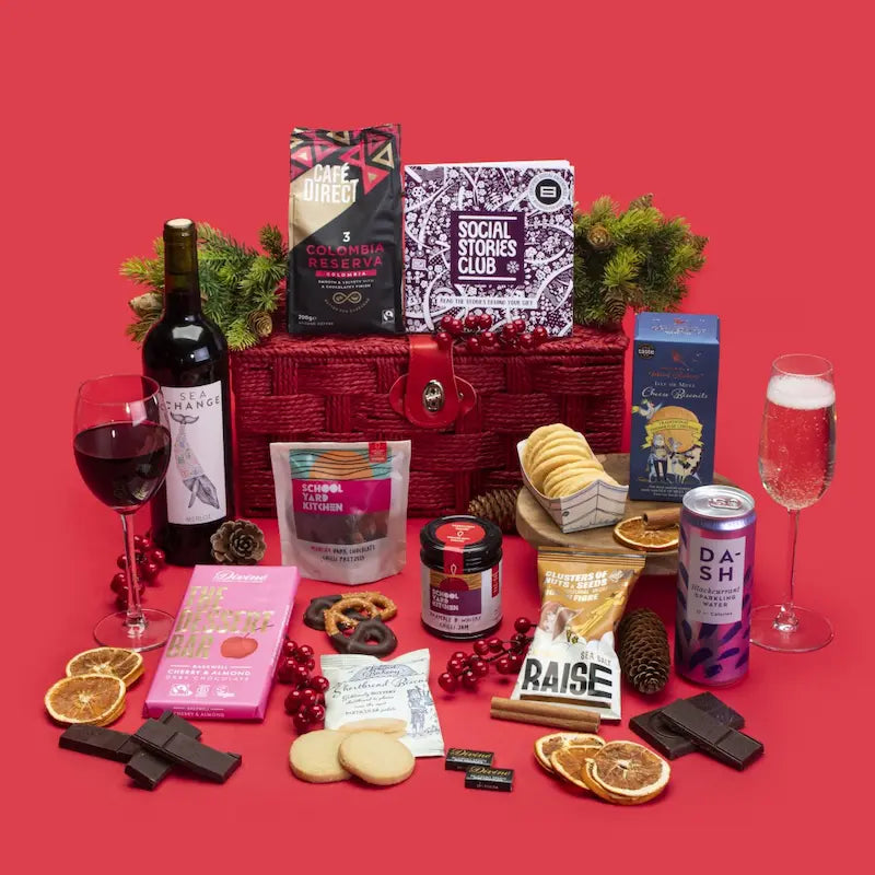 Client Thank You Gift Hamper open, displaying Colombian coffee, shortbread and cheese biscuits, dark chocolate napolitains and Bakewell, chilli pretzels and jam, salted caramel nuts, blackcurrant cordial, wine bottle, story booklet, and personalised note in elegant sustainable packaging with subtle festive accents.