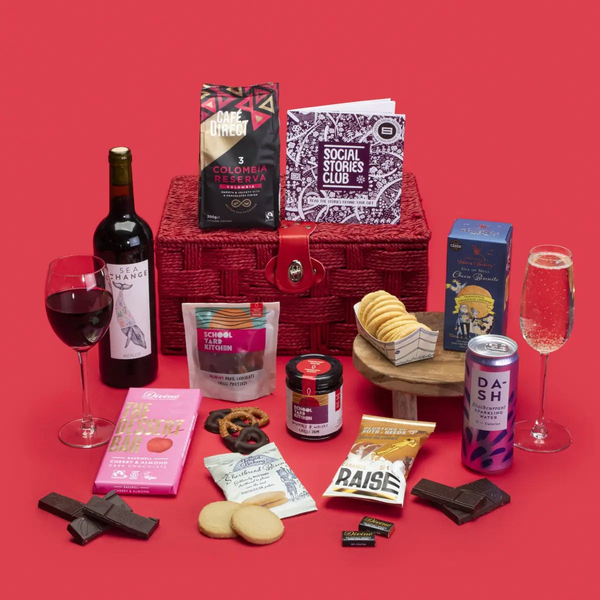 Client Thank You Gift Hamper open, displaying Colombian coffee, shortbread and cheese biscuits, dark chocolate napolitains and Bakewell, chilli pretzels and jam, salted caramel nuts, blackcurrant cordial, wine bottle, story booklet, and personalised note in elegant sustainable packaging with subtle festive accents.