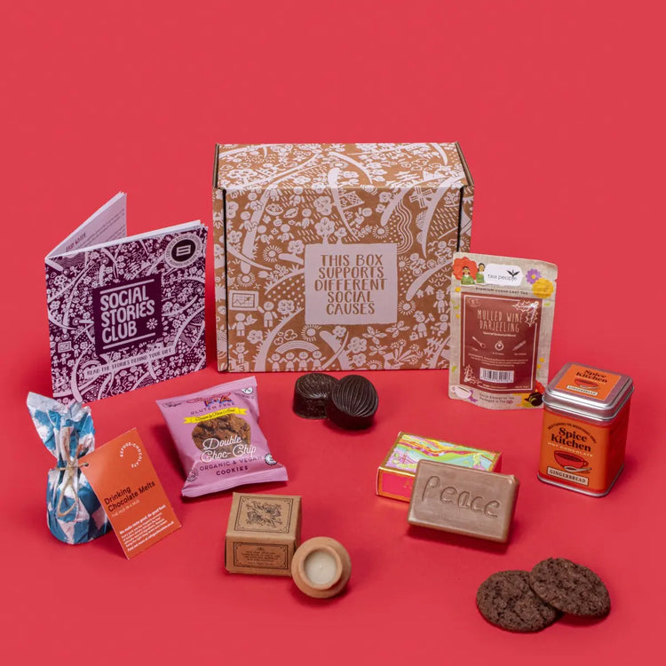 Cosy Winter Warmer Gift Box open, showcasing mulled wine tea, chocolate chip cookies, organic soap, gingerbread hot chocolate, lavender candle, and hot chocolate melts with festive pine cones and red accents.