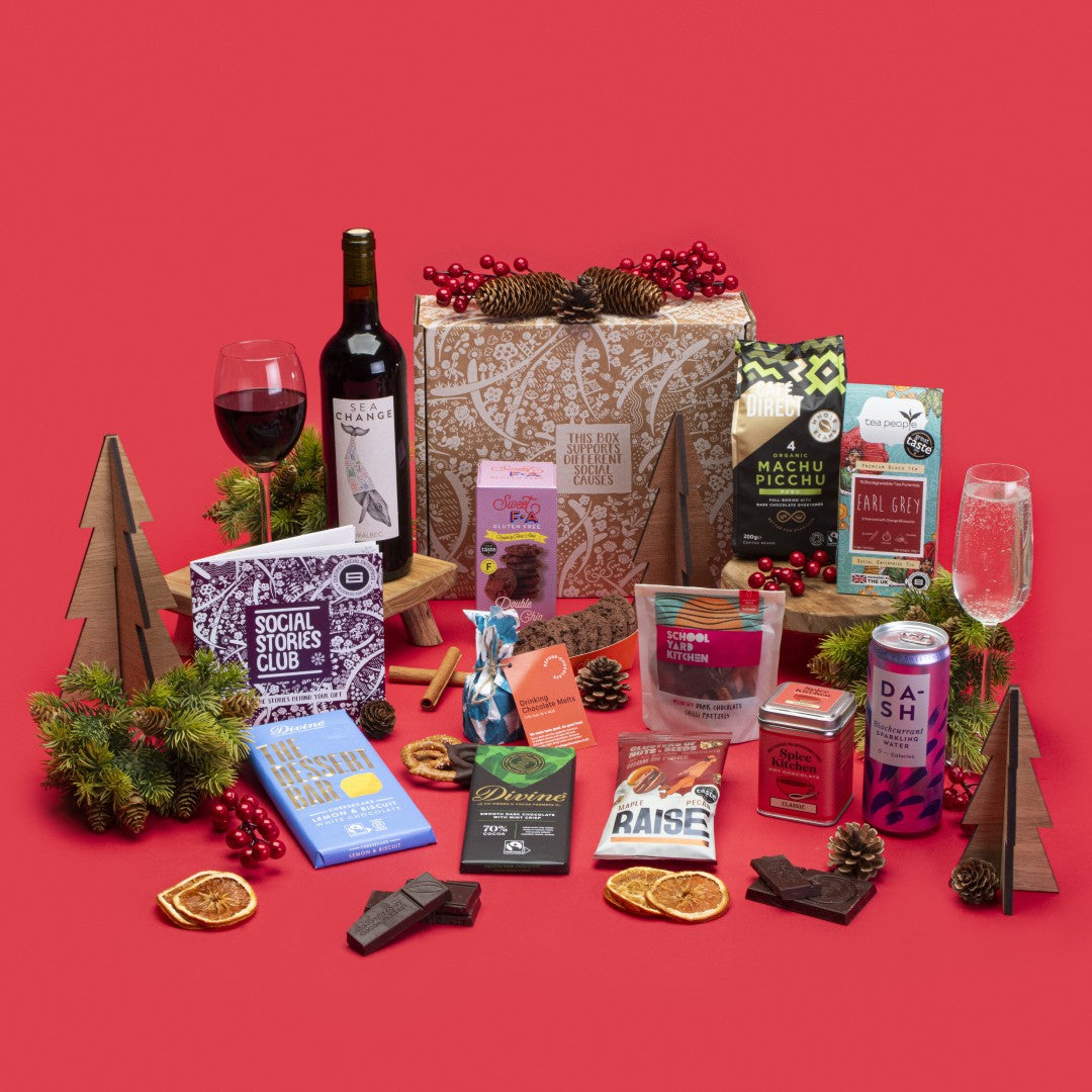 Indulgent Gift Box open, showcasing Earl Grey tea, Machu Picchu coffee, double chocolate cookies, white chocolate lemon cheesecake bar, fruit and nut dark chocolate, hot chocolate, chilli pretzels, maple pecan nuts, blackcurrant sparkling water, hot chocolate melts, wine, story booklet, and personalised note in eco-luxe packaging.