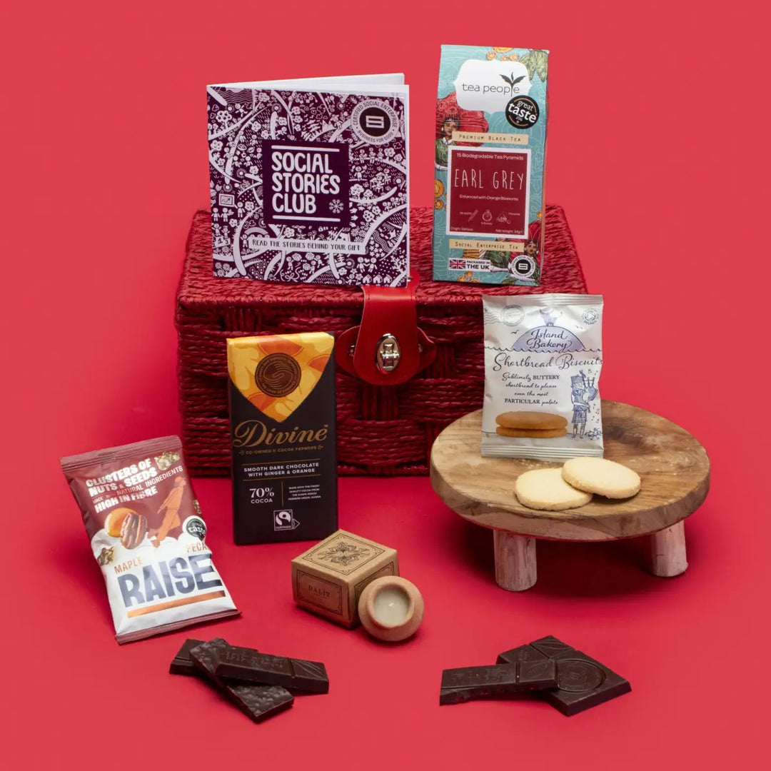 Social Impact Gift Hamper open, displaying Earl Grey tea, twin-pack shortbread, ginger orange dark chocolate, lavender candle, maple pecan nuts, story booklet & personalised note in luxurious sustainable packaging with festive accents.