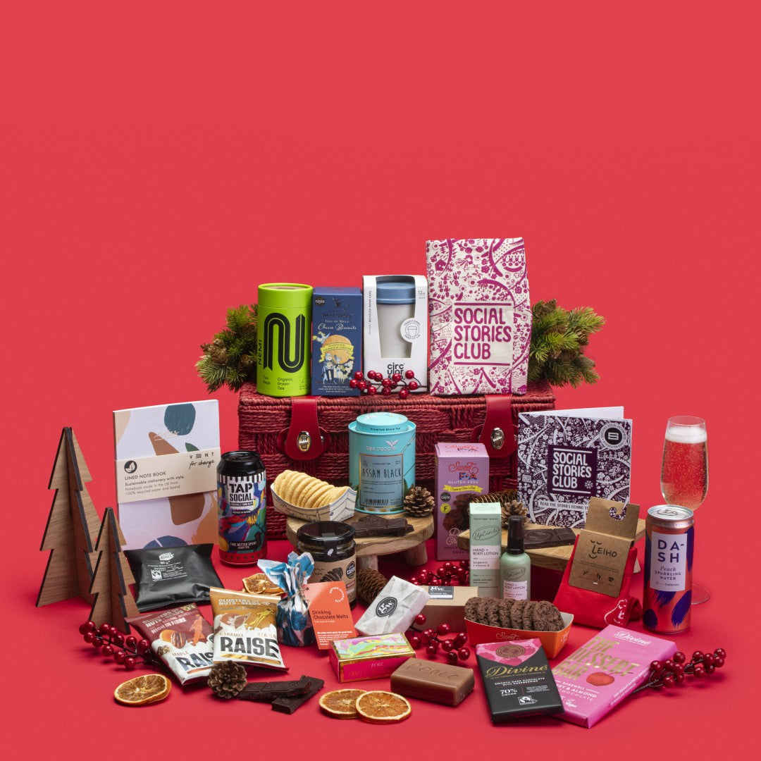 Ultra Impact Gift Hamper open, showcasing Assam tea caddy, filter coffee, cheese biscuits, chocolate chip cookies, organic soap, raspberry and Bakewell dark chocolates, maple pecans, salted caramel nuts, honey, peach sparkling water, shampoo bar, cotton tote, A5 notebook, green tea, hot chocolate melts, bamboo socks, bergamot lotion, coffee cup, IPA, story booklet, and personalised note in opulent sustainable packaging with impactful festive accents.