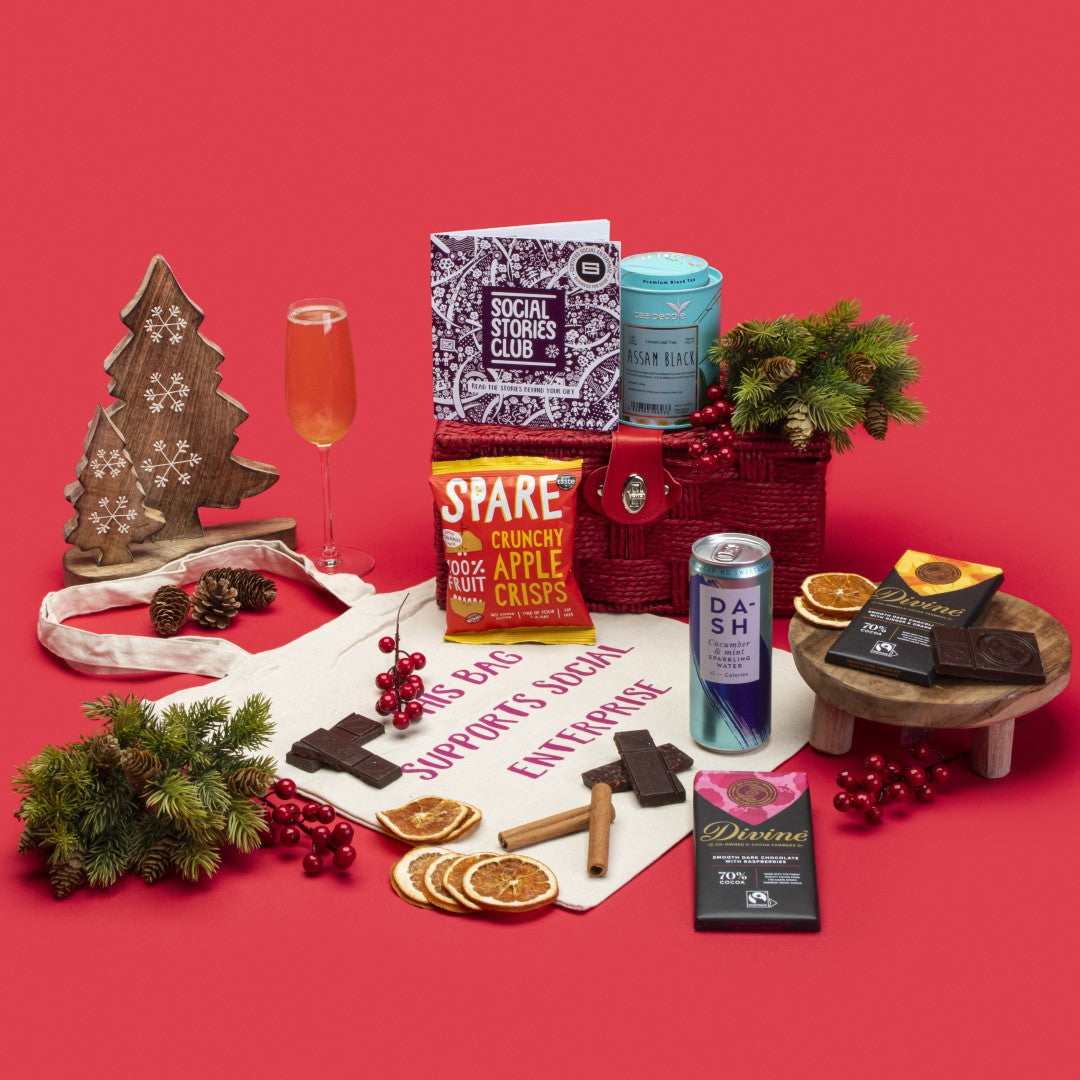 Vegan Treats Gift Hamper open, showcasing Assam tea caddy, raspberry and ginger orange dark chocolates, apple crisps, cucumber sparkling water, cotton tote bag, story booklet, and personalised note in elegant sustainable packaging with festive Christmas accents.